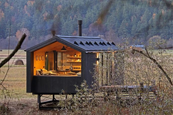 A black-clad tiny home rises above the ground on a metal frame