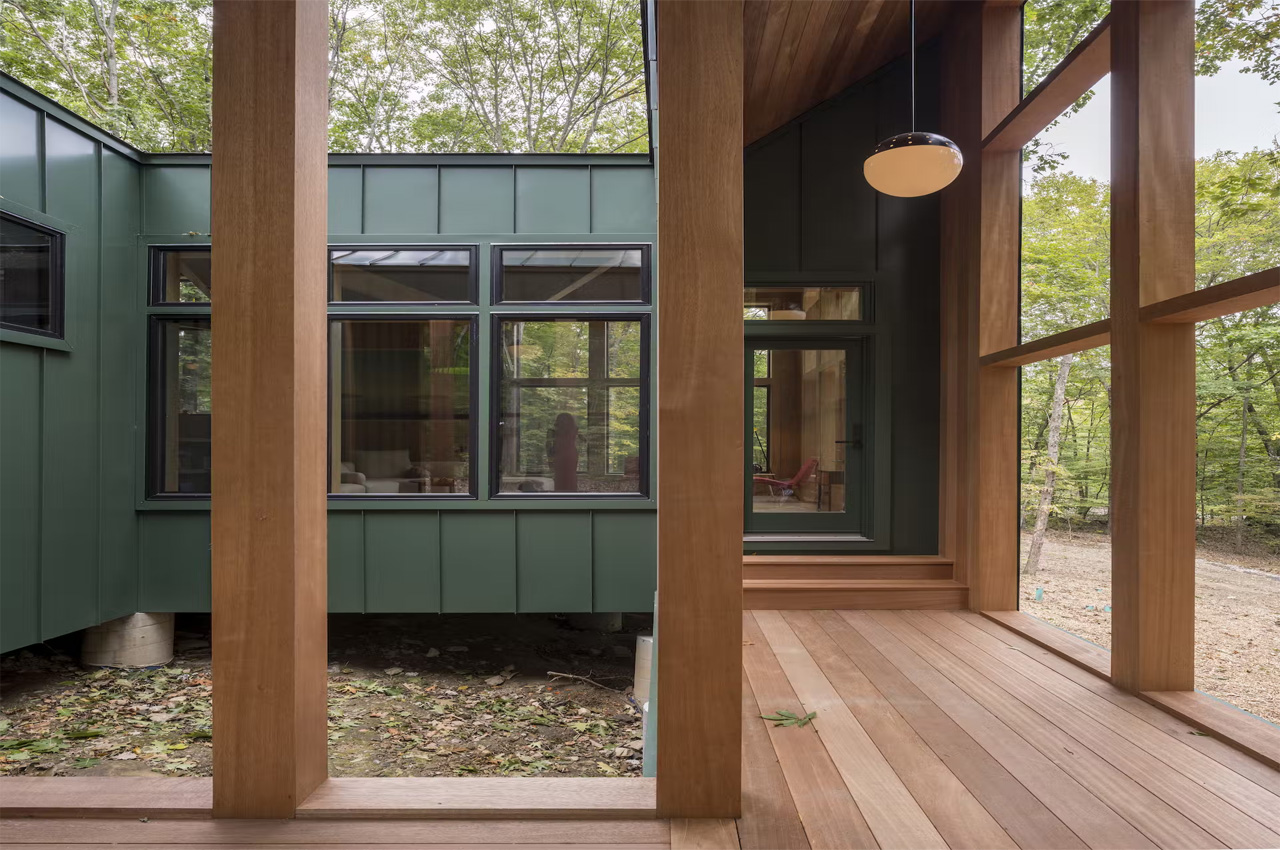 This dark green cabin floats above a sloping terrain in a forest in Connecticut