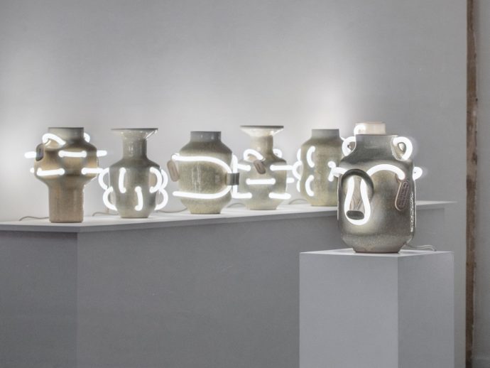Ceramic jars with neon tube lights cast an eerie glow that blends past and present