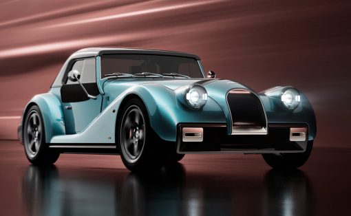 Teal blue vintage convertible with large rounded headlights and chrome grille, parked on a reflective surface.