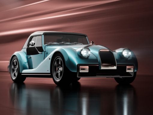 Teal blue vintage convertible with large rounded headlights and chrome grille, parked on a reflective surface.