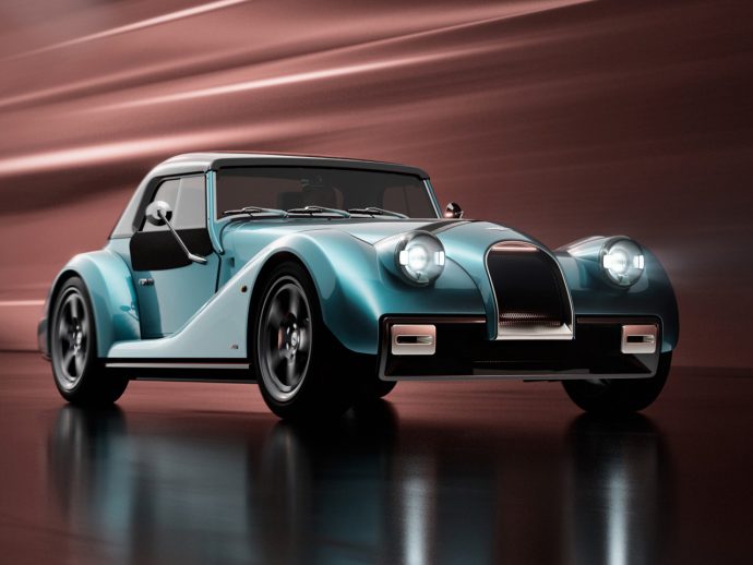 Teal blue vintage convertible with large rounded headlights and chrome grille, parked on a reflective surface.