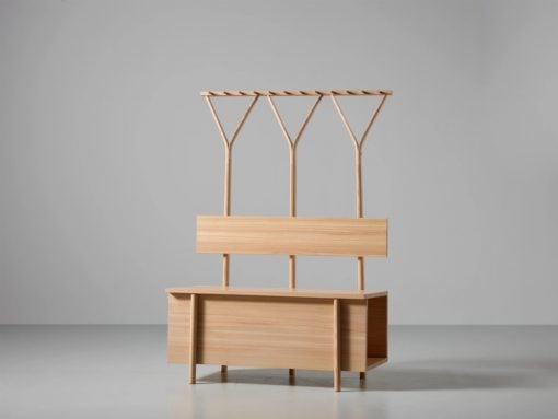 Wooden hall tree with three Y-shaped coat hooks above a bench and storage cabinet at the base, all in light oak finish