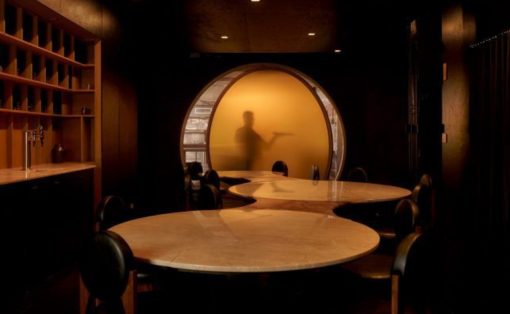 Dim restaurant interior with round marble tables and a glowing circular doorway showing a blurred staff figure in a yellow glow.