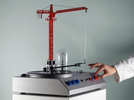 Red construction-crane model mounted on a silver rotary platform, with a hand turning a red control knob on the panel.