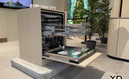 Open built-in dishwasher on display in a showroom, with its lower rack pulled out and interior racks visible.