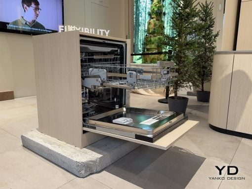 Open built-in dishwasher on display in a showroom, with its lower rack pulled out and interior racks visible.