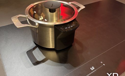 Stainless steel pressure cooker with glass lid on a black induction base.