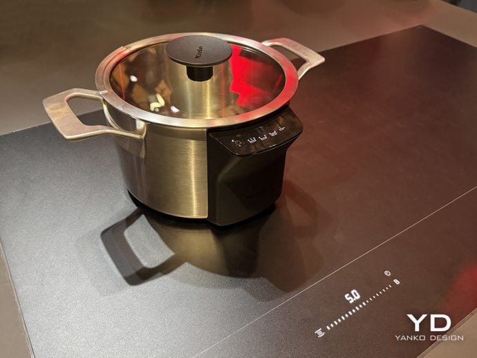 Stainless steel pressure cooker with glass lid on a black induction base.