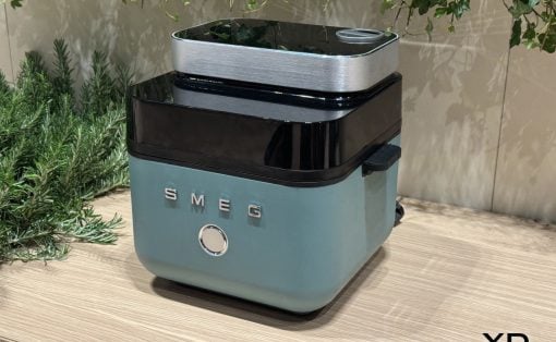 Retro teal SMEG toaster with chrome trim on a wooden counter, greenery in the background.