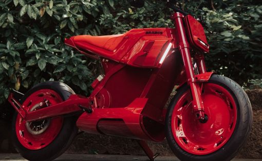 Bright red Brabus sport motorcycle parked on pavement with green shrubbery behind it.