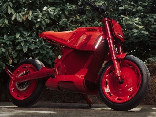 Bright red Brabus sport motorcycle parked on pavement with green shrubbery behind it.