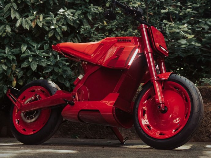 Bright red Brabus sport motorcycle parked on pavement with green shrubbery behind it.