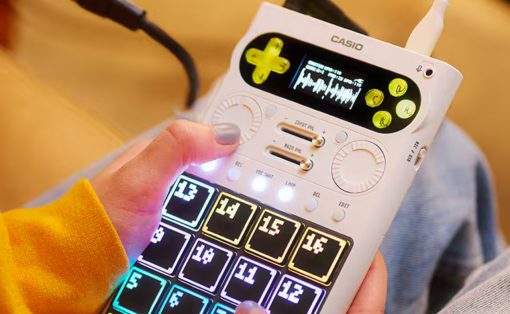 Person holding a white Casio portable music device with a colorful, glowing 4x4 pad grid to trigger sounds.