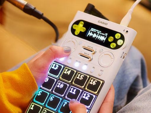 Person holding a white Casio portable music device with a colorful, glowing 4x4 pad grid to trigger sounds.