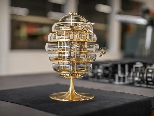 Ornate brass-and-glass egg-shaped timepiece on a gold stand, displayed on a dark table cloth.