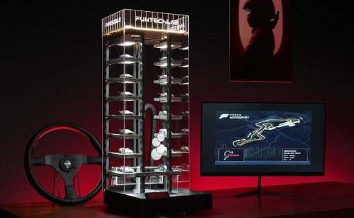 Glass multi-level car display case filled with miniature race cars, with a red-lit racing wheel and a monitor showing a Forza Motorsport race map.
