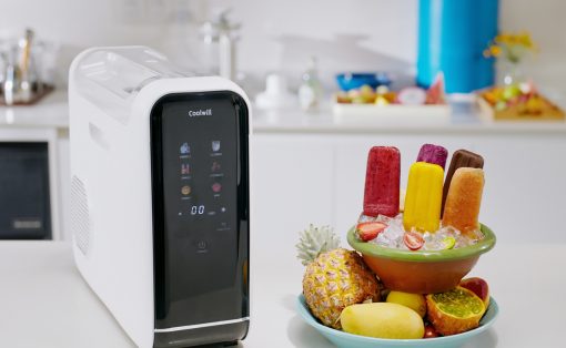 White Coolwill ice cream maker on a clean kitchen counter beside a colorful fruit and popsicle bowl.
