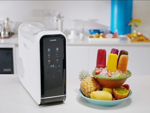 White Coolwill ice cream maker on a clean kitchen counter beside a colorful fruit and popsicle bowl.