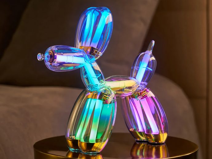 Colorful illuminated balloon-dog sculpture made of glass-like tubes, glowing in blue, green, purple, and pink on a gold pedestal.
