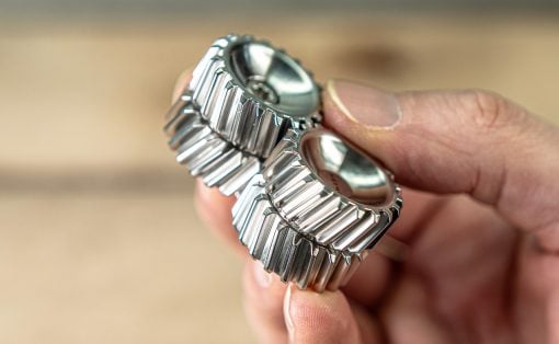 Close-up of a person's fingers holding two silver metal watch bands with interlocking links.