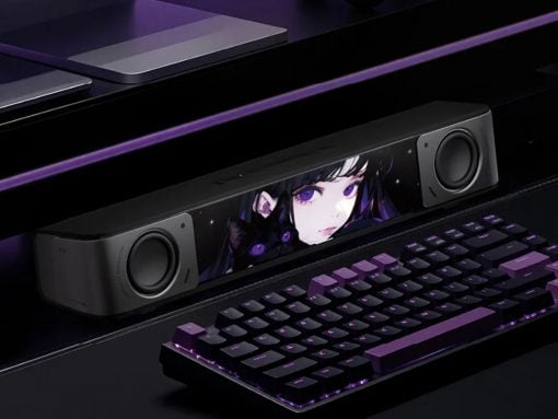 Gaming setup with a black soundbar showing anime artwork, flanked by two speakers and a purple-backlit keyboard.