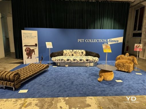 Exhibit booth with a blue backdrop reading 'PET COLLECTION by Elanco'; a dalmatian‑print sofa center stage, flanked by a dark fur chair and a round-topped table on blue carpet.