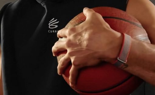 Person holding a red basketball against their chest with both hands, wearing a black sleeveless hoodie and a gray wristband
