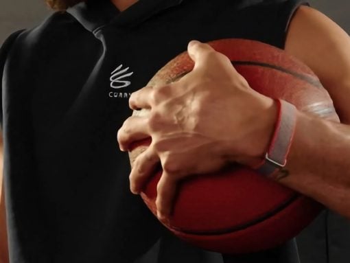 Person holding a red basketball against their chest with both hands, wearing a black sleeveless hoodie and a gray wristband