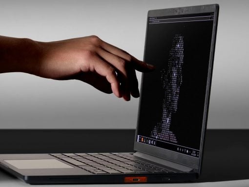 Close-up of a hand reaching toward a laptop screen displaying a fingerprint-shaped pattern made of code characters.