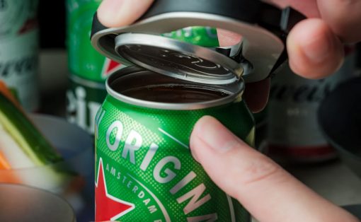 Hands open a green canned beverage using the pull-tab, lid lifted off the top.