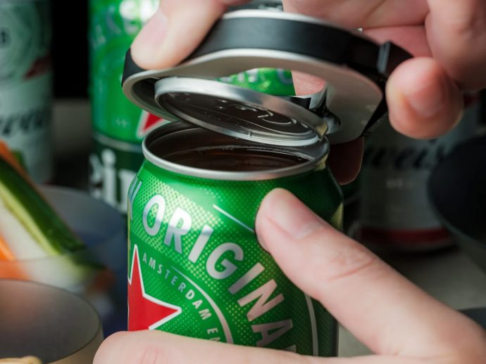 Hands open a green canned beverage using the pull-tab, lid lifted off the top.