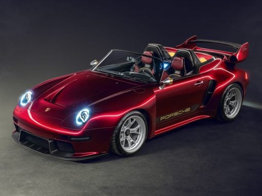 Red Porsche convertible sports car with open top, sleek headlights, and a large rear wing in a studio setting with a dark backdrop.