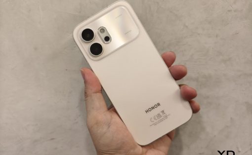 White Honor smartphone held in a hand, showing the rear camera module at the top-left and the HONOR logo toward the bottom on a light background with a watermark in the corner.