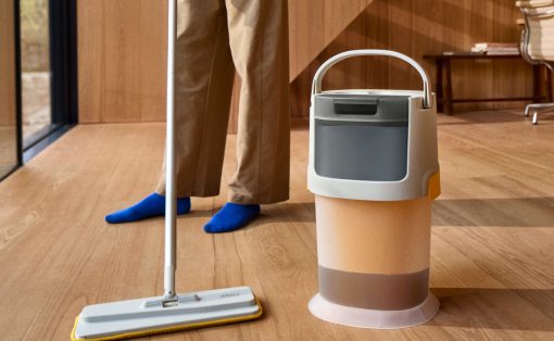Person mopping a wooden floor with a flat mop, with a beige bucket beside them.
