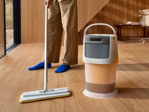 Person mopping a wooden floor with a flat mop, with a beige bucket beside them.