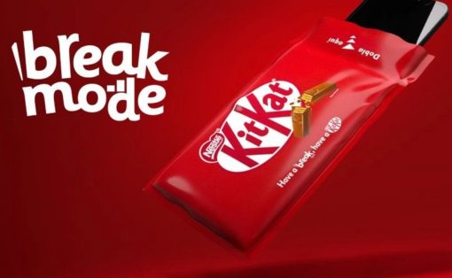 Red KitKat chocolate bar partially out of a red wrapper with a smartphone seen, against a red background, advertising the slogan 'break mode'.