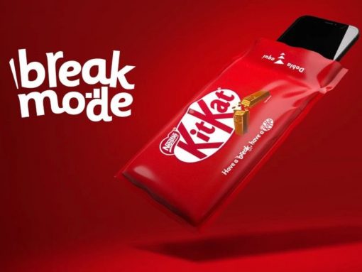 Red KitKat chocolate bar partially out of a red wrapper with a smartphone seen, against a red background, advertising the slogan 'break mode'.