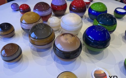 Assorted glossy, dome-shaped containers in multiple colors arranged on a white table at a design exhibit.
