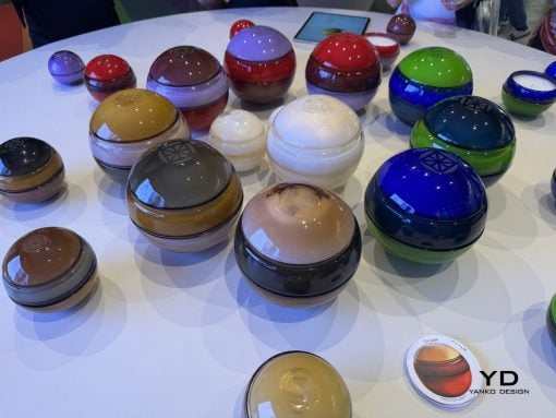 Assorted glossy, dome-shaped containers in multiple colors arranged on a white table at a design exhibit.