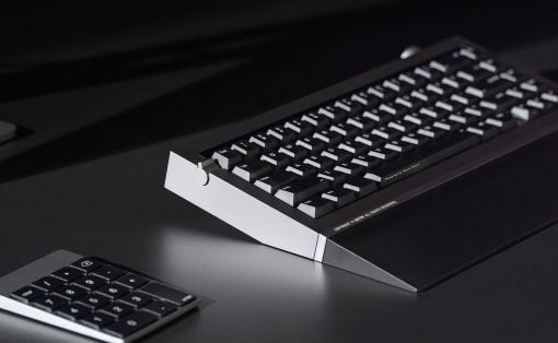 Retro computer keyboard with an angled white stand on a dark desk, plus a small numeric keypad nearby.