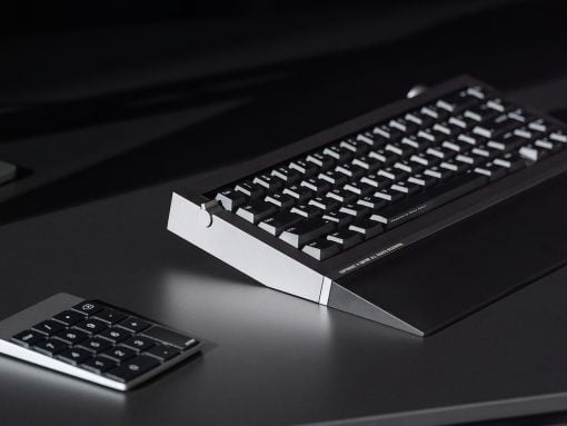 Retro computer keyboard with an angled white stand on a dark desk, plus a small numeric keypad nearby.