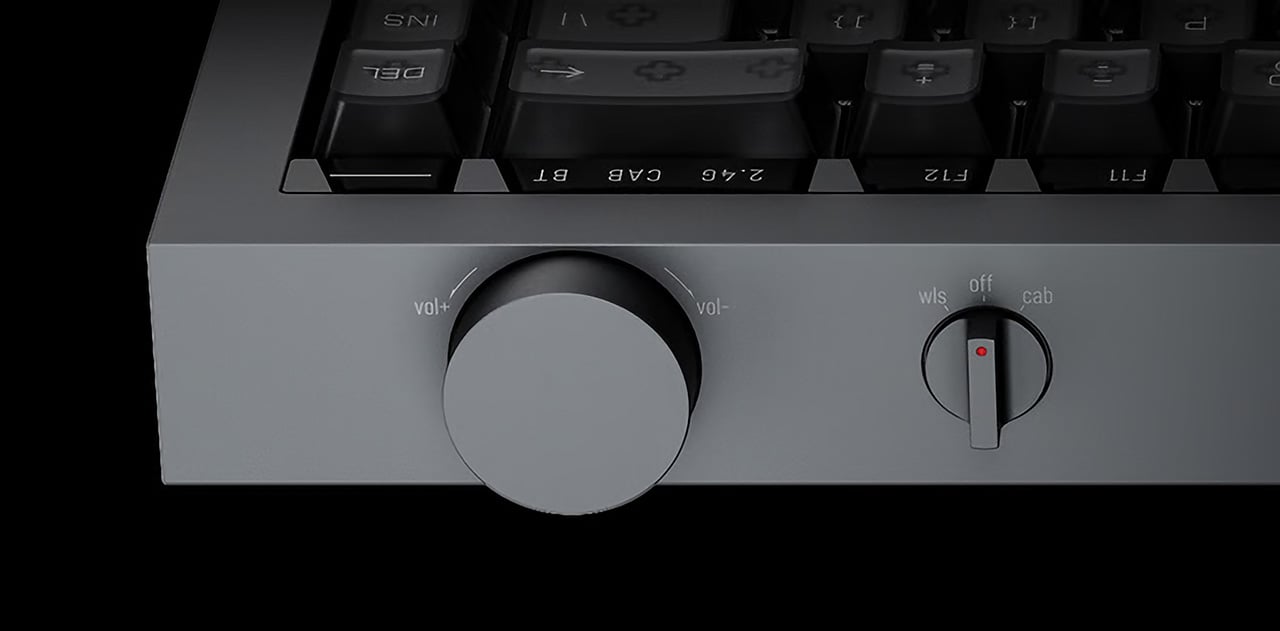 Close-up of a gray audio receiver front panel showing a large round volume knob and a smaller mode switch with a red indicator.
