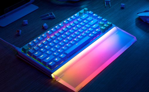 RGB-lit mechanical keyboard with multicolor underglow on a desk, surrounded by peripherals like headphones and a laptop.