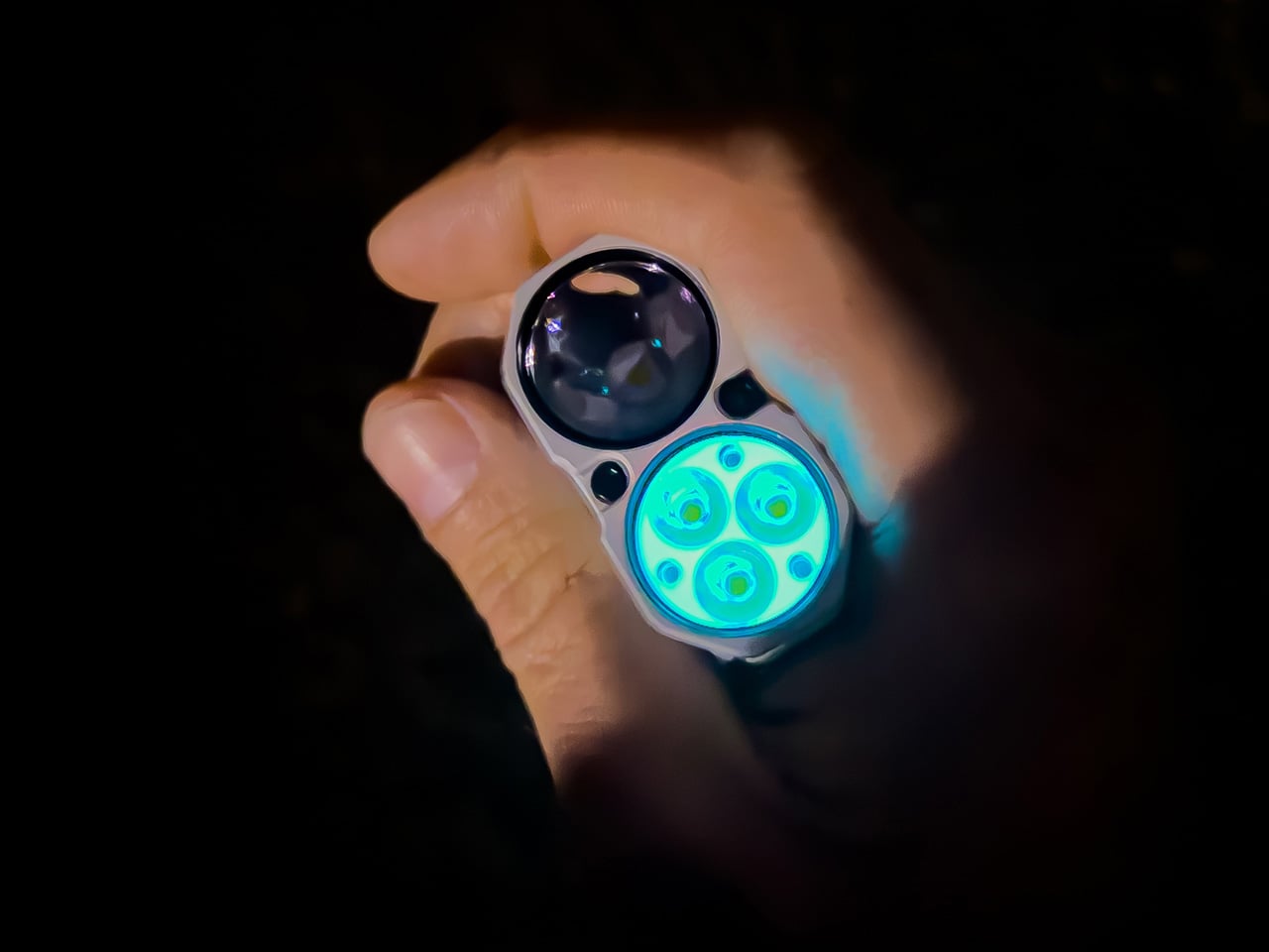 Person holding a small flashlight with blue glowing circular LEDs in a dark background.