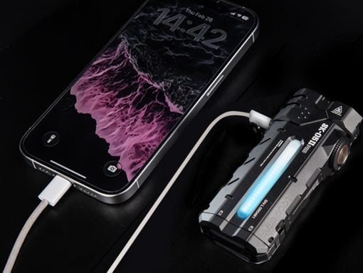 Smartphone connected to a rugged electronic device via a charging cable on a dark surface, blue glow from the device visible.