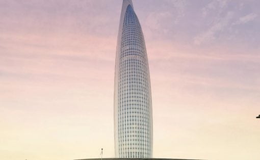 Tall, oval skyscraper with a curved glass facade rising from a circular plaza at sunset.