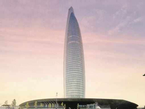 Tall, oval skyscraper with a curved glass facade rising from a circular plaza at sunset.