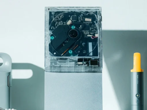 Transparent computer case opened to reveal internal circuitry and a visible hard drive, with a yellow-handled tool nearby on a light surface.