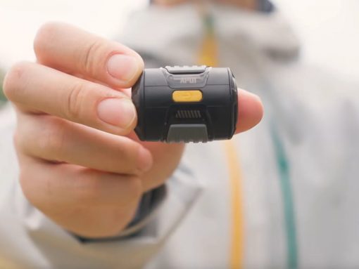 Close-up of a hand holding a small black wearable device with a yellow button on top.